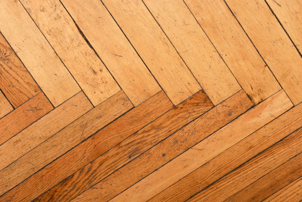 Close-up of a wooden floor with a herringbone pattern, showing the surface detail relevant to scratch repair